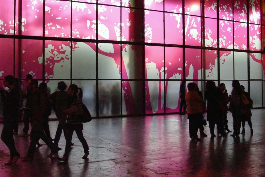 Público circula diante de painel de vidro iluminado em rosa na entrada da São Paulo Fashion Week